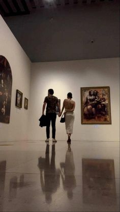 two people standing in an art gallery looking at paintings