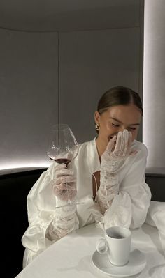 a woman sitting at a table with a glass of wine in front of her face