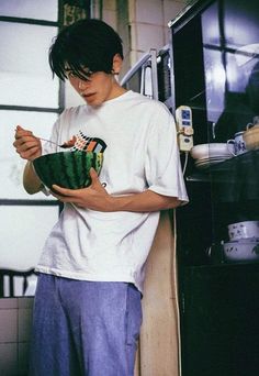 a man standing in front of an oven holding a bowl and looking at his cell phone