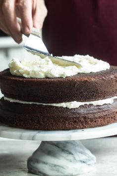 someone is cutting into a chocolate cake with white frosting