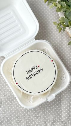 a birthday cake in a plastic container with the words happy birthday written on it next to a potted plant