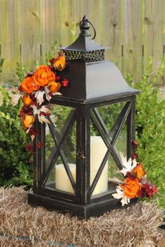 a black lantern with orange and red flowers on it sitting in front of some bushes