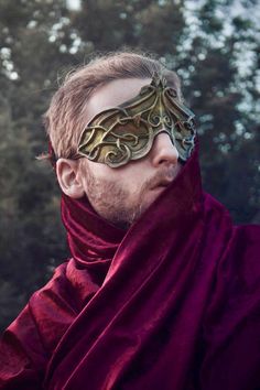 a man with a mask on his face wearing a red cape and scarf around his neck