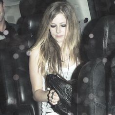 a woman sitting in the back seat of a car holding a purse and looking at her cell phone