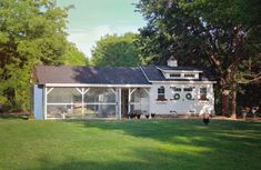 a small white house sitting on top of a lush green field next to tall trees