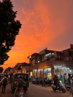 the sky is pink and orange as people are walking down the street in front of motorcycles