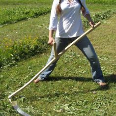 a woman standing in the grass holding a long stick and wearing jeans with her hands behind her back