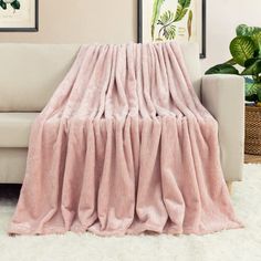 a couch with a pink blanket on it in a living room next to a potted plant