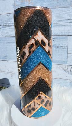 a blue, brown and black vase sitting on top of a white pedestal next to a wooden wall