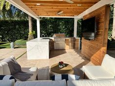 an outdoor kitchen and grill area with white couches under a pergolated roof