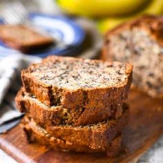 three slices of banana bread on a wooden cutting board with bananas in the back ground