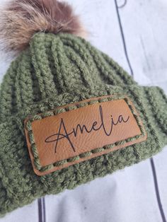 a green hat with a name tag and a fur pom - pom on it