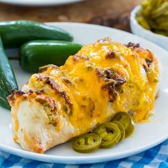 a white plate topped with chicken and green peppers next to pickles on a table