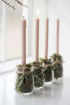 four candles are lined up in small glass jars with moss and pine cones on them