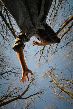 a person is reaching up into the sky from below, with bare trees in the foreground