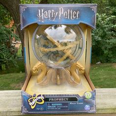 a harry potter prophecy clock in its box on a wooden table with trees in the background