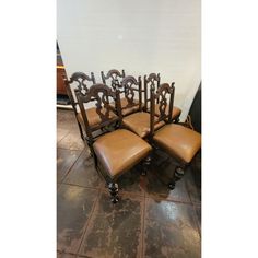 a set of four chairs with brown leather seats and carved wood frames on the back