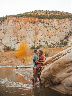 an engaged couple embraces in the water near a cliff