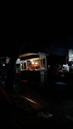 people are standing outside at night by the food stand that is lit up in the dark