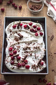 a cake with white frosting and cherries in a pan on a wooden table