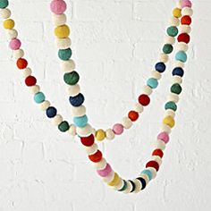 multicolored beaded necklaces hanging on a white brick wall in an art gallery