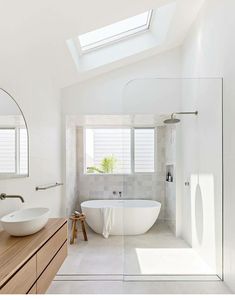 a white bathroom with a skylight above the bathtub and two sinks in front of it