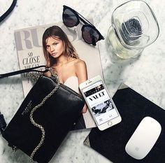 a cell phone is sitting on top of a magazine next to sunglasses and a purse