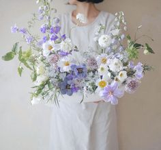 a woman holding a bouquet of flowers in her hands and wearing a white dress with black hair