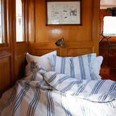 there is a bed with blue and white striped sheets on it in the room that has wood paneling