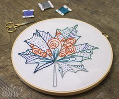 the embroidery is being worked on by someone using scissors and needle tips to make an embroidered maple leaf