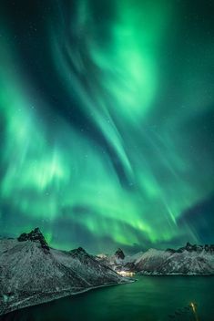 the aurora bore is shining brightly in the night sky over mountains and lake with snow on them