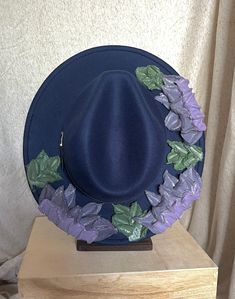 This one of a kind, hand painted, textured floral fedora is the perfect walking art piece. Each hat is uniquely crafted and perfect for any occasion.  This navy blue fedora is crafted with soft glittered purples, lavender, and green accents. These island treasures are shipped straight to you from the Hawaiian island of Oahu. (Hats are water resistant. Keep out of heavy rain. Spot clean only) Blue Hat For Kentucky Derby Festival, Blue Hat For Kentucky Derby, Blue Adjustable Fedora For Kentucky Derby, Blue Bohemian Fedora For Spring, Bohemian Blue Fedora For Spring, Blue Fedora With Curved Brim For Festival, Artistic Fedora With Short Brim For Spring, Whimsical Blue Wide Brim Hat, Whimsical Blue Wide-brim Hat