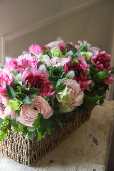 a basket filled with lots of pink flowers on top of a wooden table next to a window