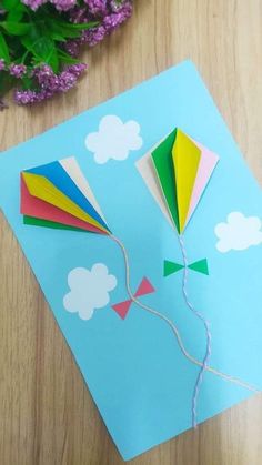 a colorful kite is on top of a blue card with flowers in the back ground