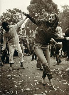 a woman is dancing in the middle of a group of people on a dirt field