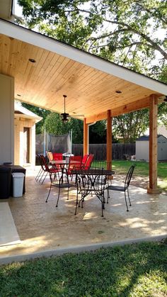 a covered patio with tables and chairs under a tree in the back yard, next to a fire pit