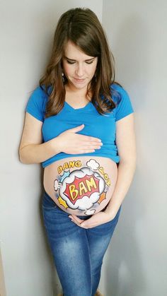 a pregnant woman is holding her belly in the shape of a superman symbol, while standing against a wall