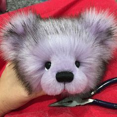 a person holding a small stuffed animal with scissors in it's hand, on top of a red blanket