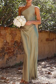 a woman in a green dress holding a white bouquet and standing next to a stone wall