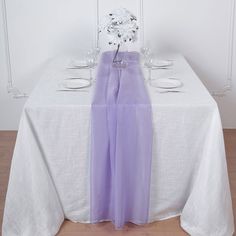 a white table topped with a vase filled with flowers next to two empty glasses and plates