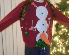 a man wearing a snowman sweater standing in front of a christmas tree