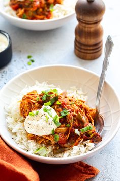 two bowls filled with rice and meat on top of a white tablecloth next to a wooden spoon