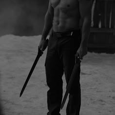 a shirtless man holding two large knives in his hand while standing on snow covered ground