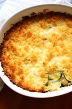 a casserole dish with cheese and zucchini in it on a wooden table