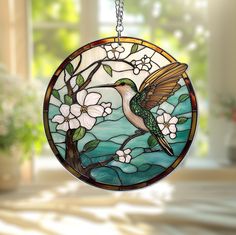 a stained glass hummingbird hanging from a window with flowers on it's side