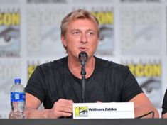 two men sitting at a table with microphones in front of them and water bottles behind them