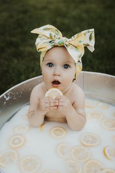 a baby in a tub with lemons and a bow on her head eating a piece of fruit