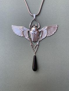 A highly detailed Egyptian Revival design dating from the 1920's featuring a winged scarab. Scarabs symbolised eternity in Egyptian mythologyThe pendant and chain are 5 micron silver plate on brass, nickel free and hypoallergenic. The 18 inch chain is included with the pendant. The measurements are 9cm wide x 7cm tall.I have also used a semi precious black Onyx drop to finish off the piece.Free worldwide shipping is included Silver Art Deco Brass Jewelry, Art Deco Silver Brass Jewelry, Silver Ankh Necklace In Brass, Vintage Silver Ankh Jewelry, Art Nouveau Silver Brass Jewelry, Medieval Vampire, Winged Scarab, Revival Design, Celtic Viking