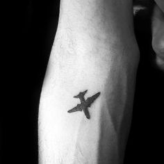 a black and white photo of a person's arm with a small airplane tattoo on it