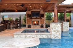 an outdoor living area with a fireplace and grill in the middle, surrounded by a swimming pool